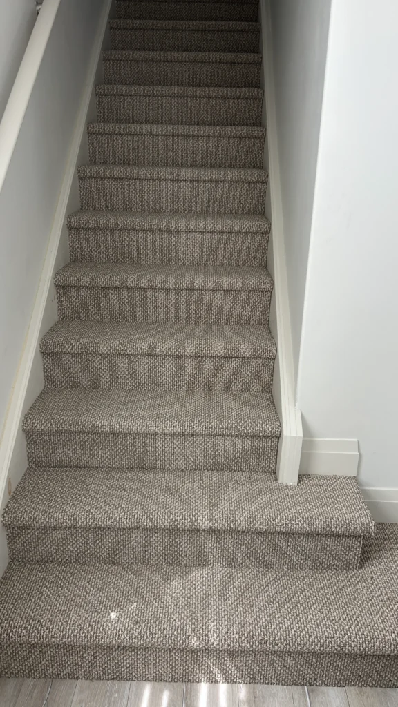 A completed staircase featuring a high-quality, beige and brown patterned carpet with professional tucking and perfectly aligned edges.