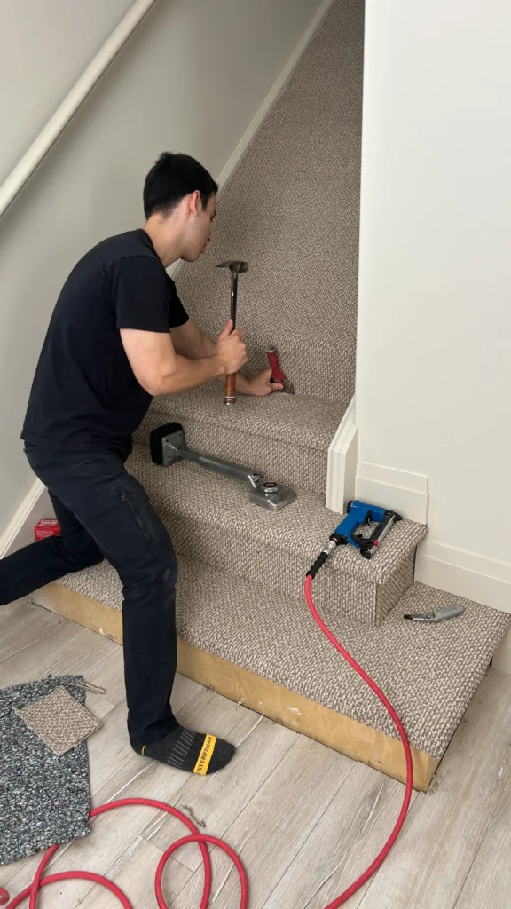 A flooring specialist using a knee kicker and carpet tucker tool to tightly secure a new patterned berber carpet onto stairs.