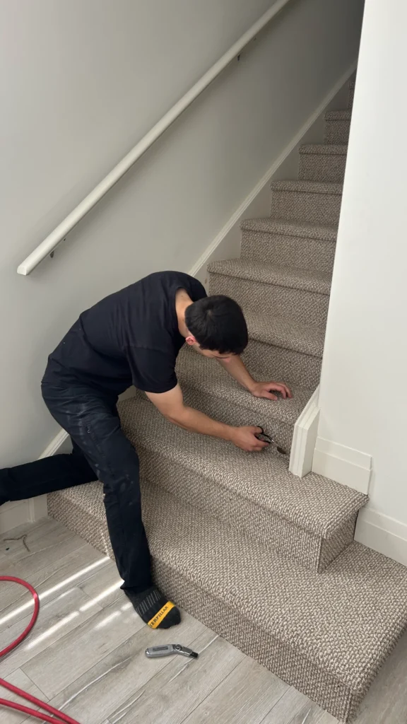 Close-up of a carpet fitter using professional cutting tools to trim excess fabric around the staircase trim for a clean, seamless look.