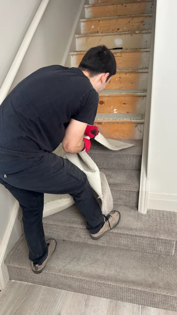 A professional flooring installer removing old, worn-out grey carpet from a wooden staircase to prepare for a new installation.